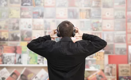 Homem usando fones de ouvido observando uma parede cheia de pôsteres de bandas clássicas.