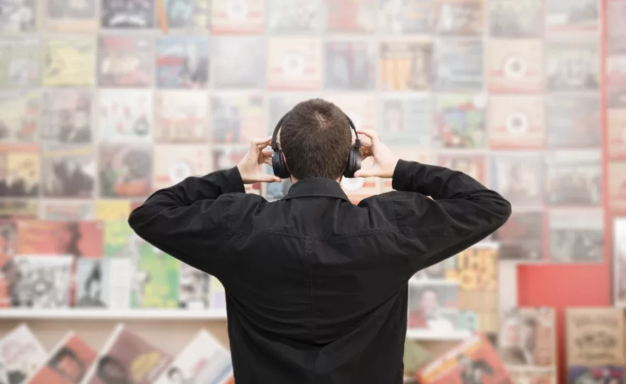 Homem usando fones de ouvido observando uma parede cheia de pôsteres de bandas clássicas.